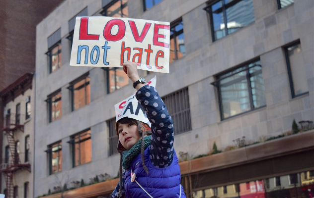 We Must Trust That a Revolution of Love Is All Around Us a young woman holding up a sign that reads: Love not Hate