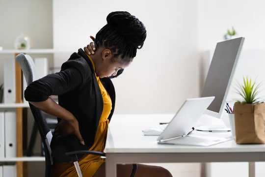 Woman sitting at desk clutches her neck and back in pain.