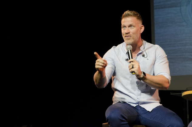 Raising My Game With Public Speaking man holding a mic, on a stage speaking dynamically