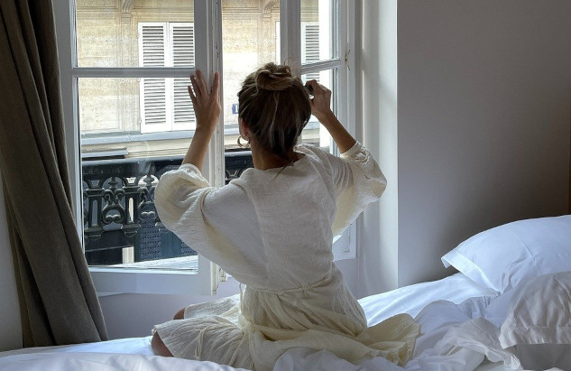 Aging Magically: Growing into a Strong Sense of Self woman sitting on the edge of her bed facing an open window